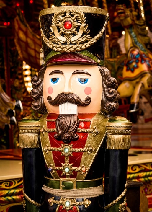 Close-up of an ornate wooden nutcracker soldier with gold trim and a carousel glowing in the background