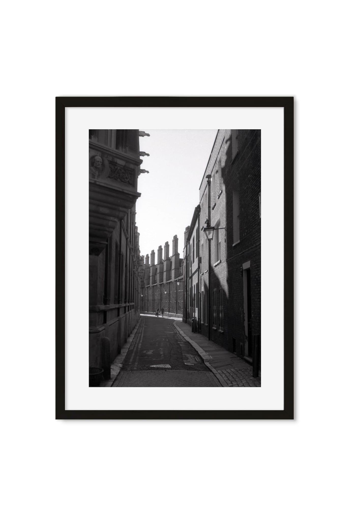 Black-and-white photo of a narrow cobblestone alley between old brick townhouses with chimney stacks