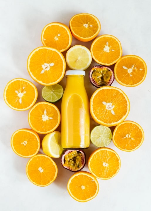 Flasche Orangensaft umgeben von halbierten Orangen, Zitrone, Limette und Passionsfrucht