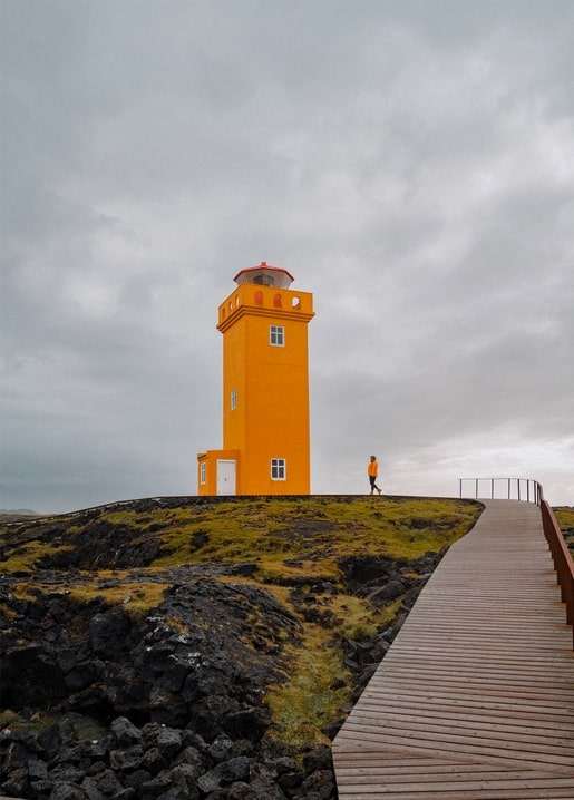 Orange lighthouse on a mossy rocky coast with a wooden boardwalk