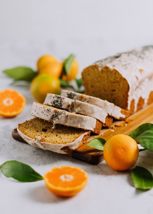 Glasierte Orangen-Stollen-Scheiben mit Mohn neben frischen Orangen