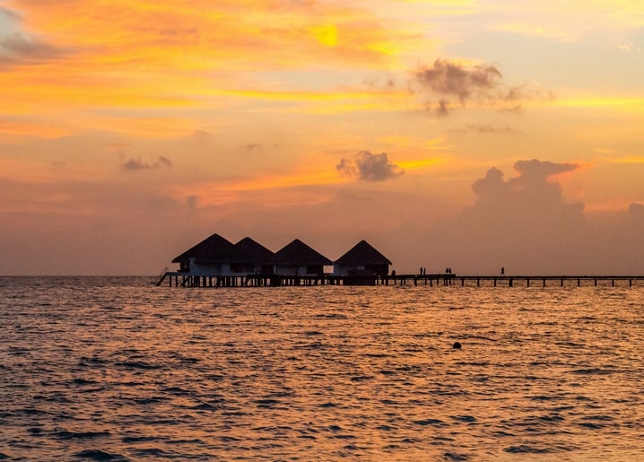 Silhouetted overwater bungalows on stilts against a golden sunset sky over a tropical sea