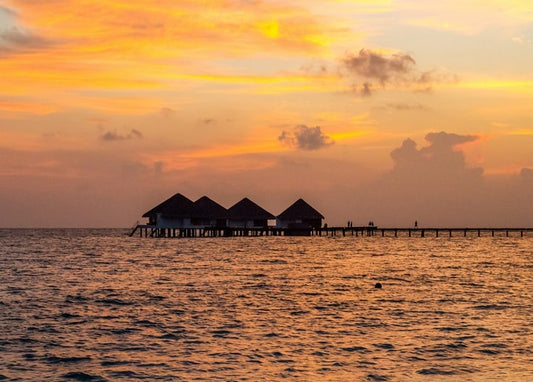 Silhouette von Überwasser-Bungalows auf Stelzen vor goldenem Sonnenuntergang über tropischem Meer