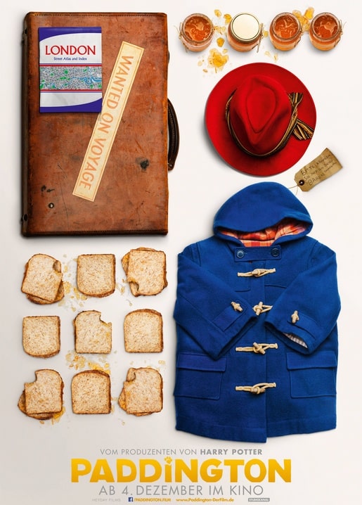 Flatlay von Paddingtons Koffer, rotem Hut, blauem Mantel, Marmelade und Toast