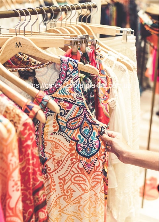 Eine Hand zieht ein buntes Paisley-Kleid aus einer Kleiderstange mit Boho-Mode.