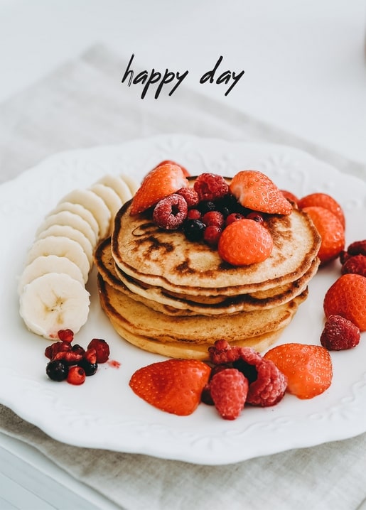 Стос млинців з бананом, полуницями та ягодами під написом «happy day»