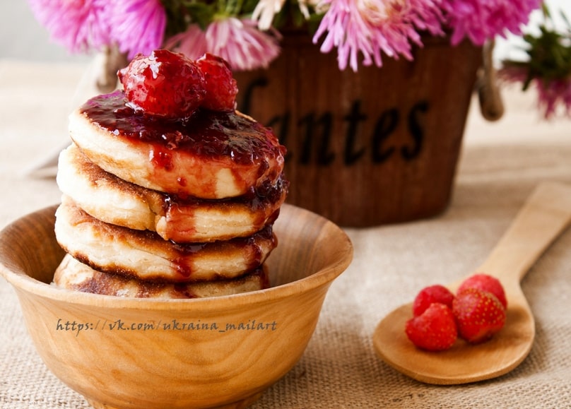 Hoher Pancake-Stapel mit Beerenkonfitüre und Himbeeren in Holzschüssel neben rosa Astern