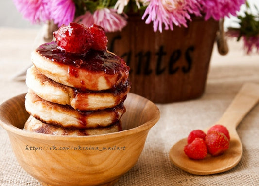 Hoher Pancake-Stapel mit Beerenkonfitüre und Himbeeren in Holzschüssel neben rosa Astern
