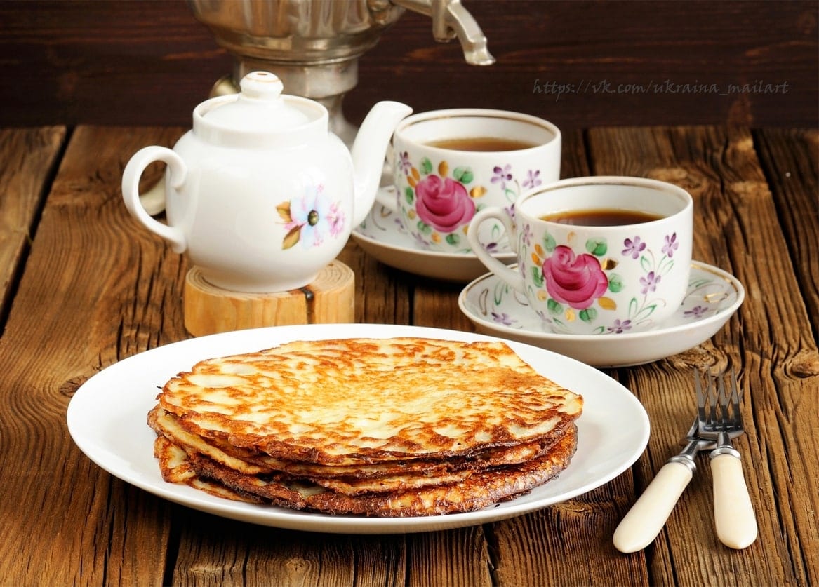 Тарілка рум'яних млинців з самоваром і чашками чаю у квіточку на дерев'яному столі