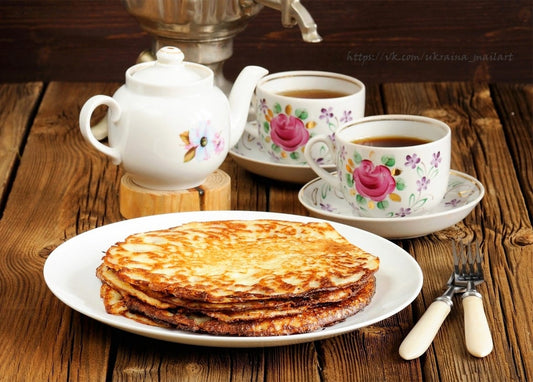 Тарілка рум'яних млинців з самоваром і чашками чаю у квіточку на дерев'яному столі