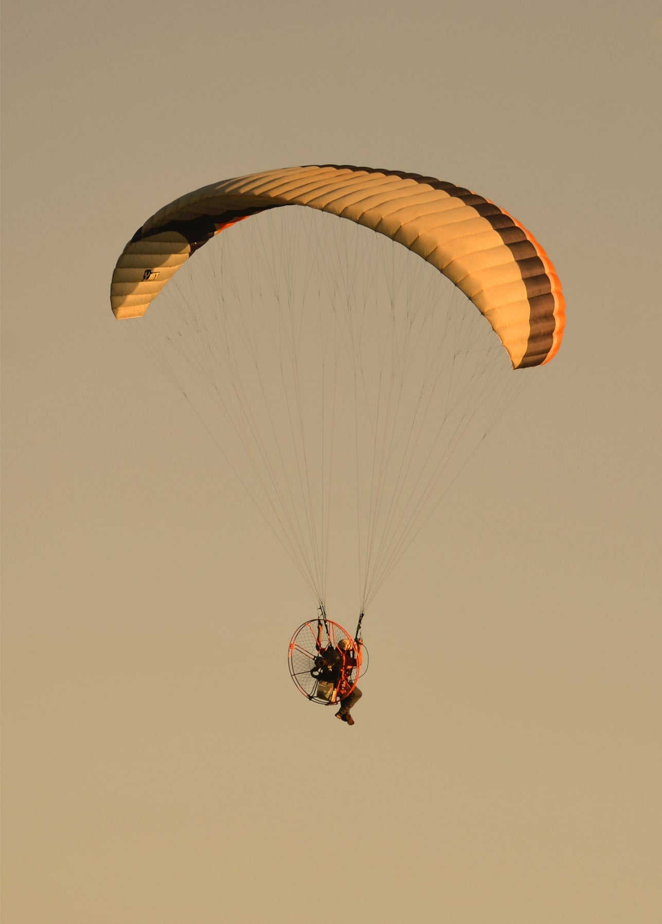Motorisierter Gleitschirm schwebt vor goldenem Sonnenuntergang