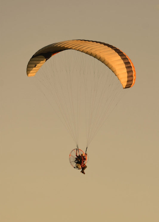 Motorisierter Gleitschirm schwebt vor goldenem Sonnenuntergang
