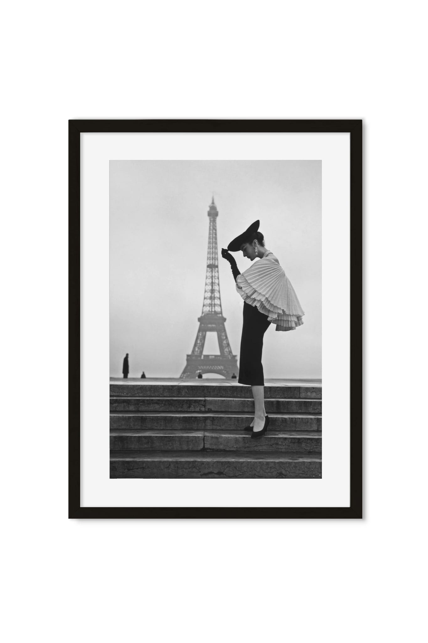 Black-and-white photo of a woman in a pleated cape and hat on steps, Eiffel Tower in the background, framed poster