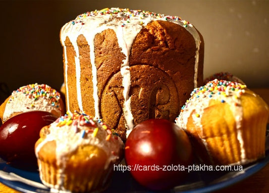 Paska Easter bread with icing and sprinkles surrounded by red eggs and mini cakes