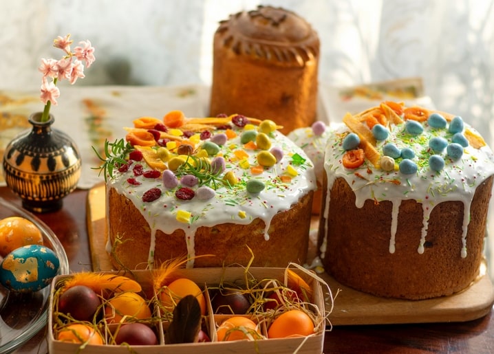 Zwei glasierte Paska-Kuchen mit Rosmarin und Pastelleiern neben einer Eierkiste in Stroh