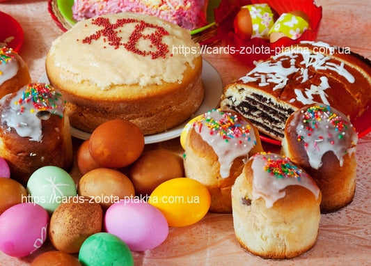 Paska iced with a Christ Is Risen message beside glazed mini buns, a chocolate babka, and brightly dyed eggs.