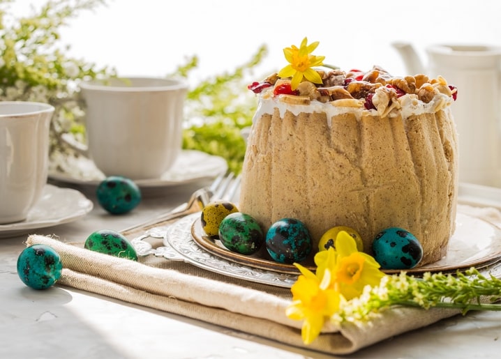 Glasierte Paska mit Walnüssen, Cranberries und Narzisse zwischen türkisen gesprenkelten Eiern und Teetassen.