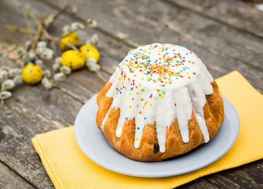 Paska with white icing drizzle and rainbow sprinkles beside pussy willow twigs