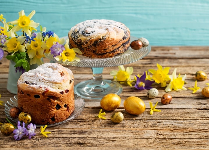 Two paska loaves with daffodils and gold, speckled quail eggs on a teal table