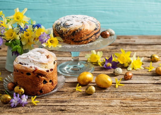 Two paska loaves with daffodils and gold, speckled quail eggs on a teal table