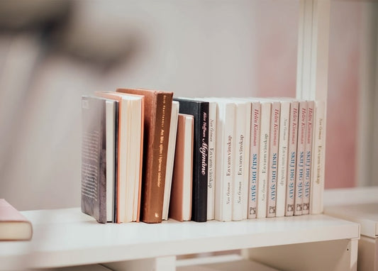 Книжки в пастельних тонах стоять рядком на білій полиці на розмитому рожевому тлі