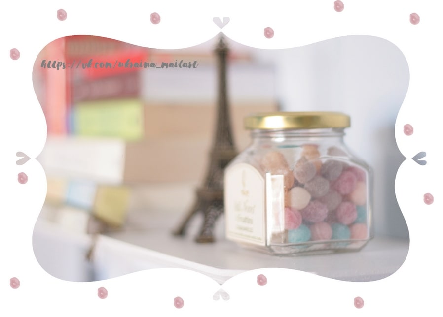 Glass jar of pastel candies beside colorful books and a small Eiffel Tower figurine