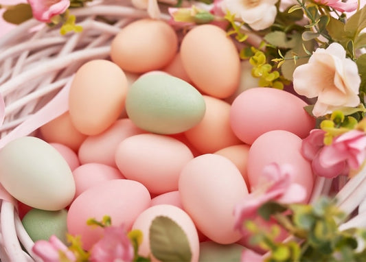 Pastel mint, peach, and pink Easter eggs nestled in a white wicker basket with pink blossoms