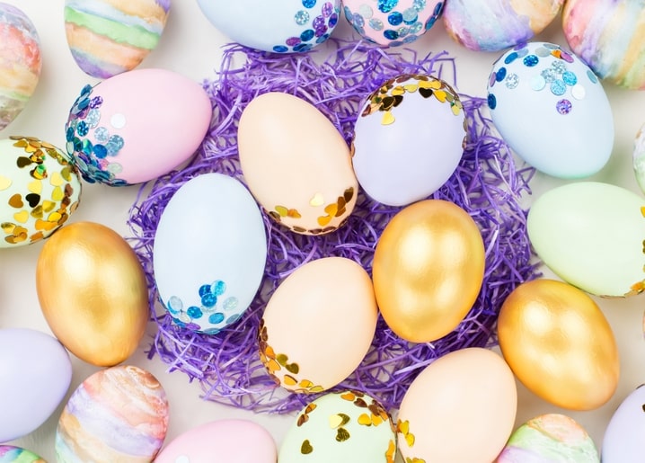 Pastellfarbene Ostereier mit Konfetti und Blattgold in einem lila Papiergras-Nest