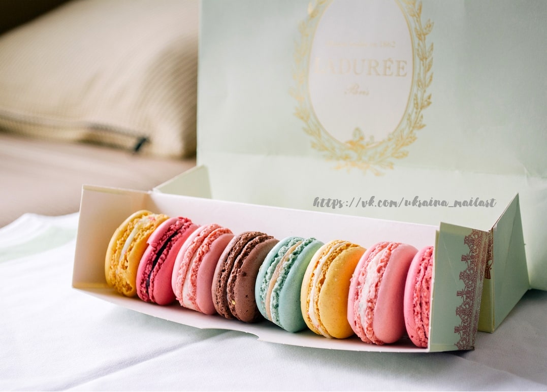 Pastellfarbene Macarons in offener Geschenkbox auf cremefarbener Bettwäsche