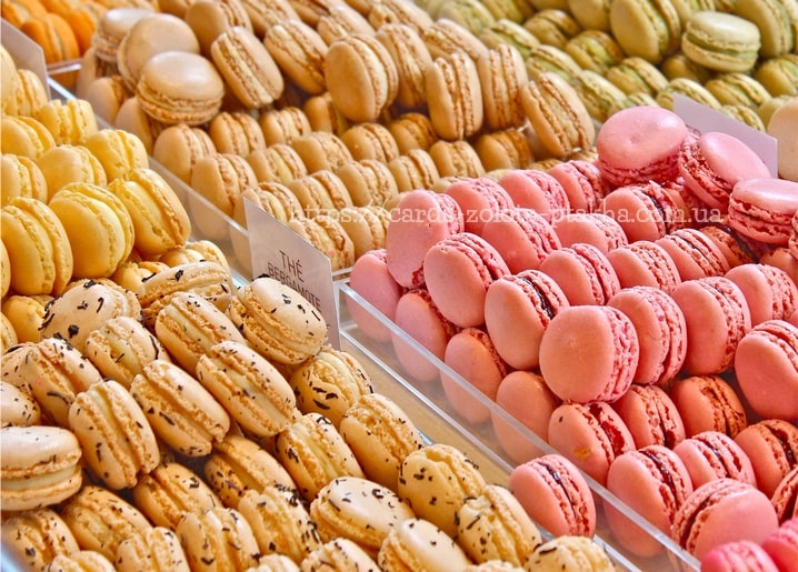 Pastellfarbene Macarons in Gelb, Rosa und Grün reihenweise in der Konditorei-Auslage