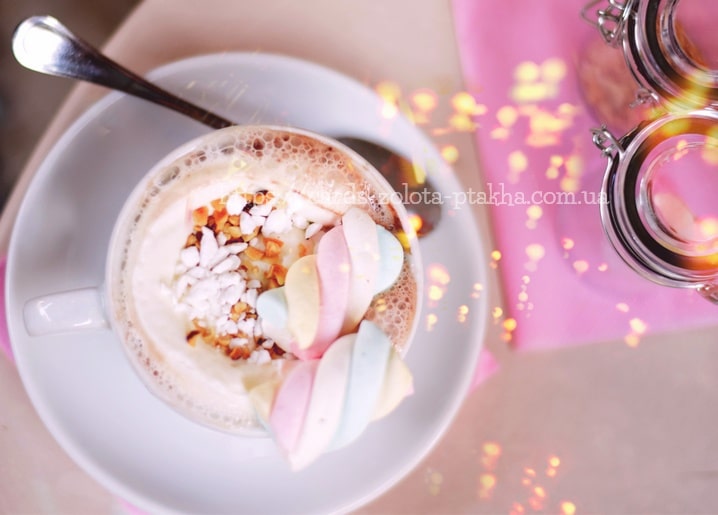 Weiße Tasse Kakao mit pastellfarbener Marshmallow-Spirale, gehackten Nüssen und funkelnden Lichtern