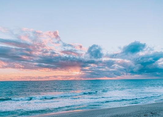 Pastellfarbene rosa-blaue Sonnenuntergangswolken über ruhigem Meer und leerem Strand