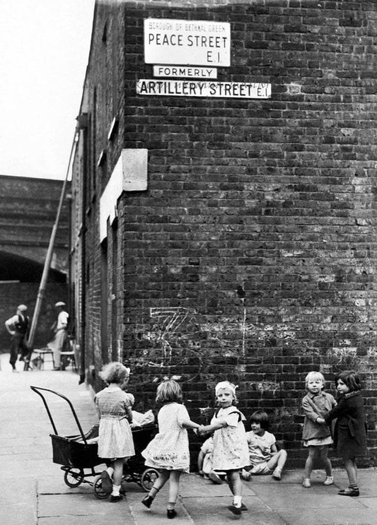 Schwarz-weißes Foto: spielende Kinder vor dem Straßenschild „Peace Street“ in London