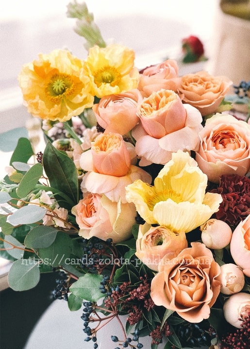 Nahaufnahme eines Straußes aus pfirsichfarbenen Rosen, gelbem Mohn und Ranunkeln mit Eukalyptusblättern