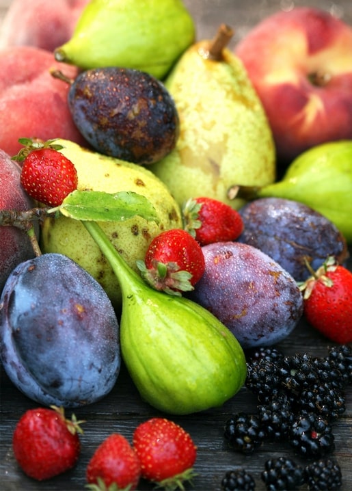 Reife Pfirsiche, Pflaumen, Birnen, Erdbeeren und Brombeeren auf einem dunklen Holztisch