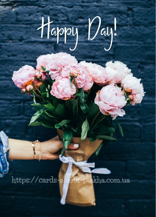 Hand hält einen Pfingstrosenstrauß in Packpapier vor einer dunklen Ziegelwand mit der Aufschrift „Happy Day!“