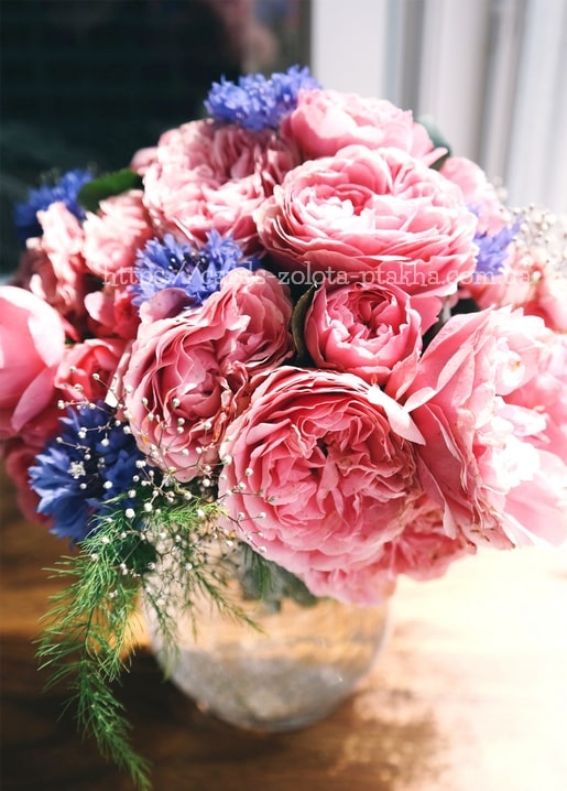 Strauß aus rosa Gartenrosen und Kornblumen in einem Glas auf der Fensterbank