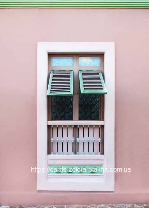 Pastel pink wall with a white window and open mint-green shutters