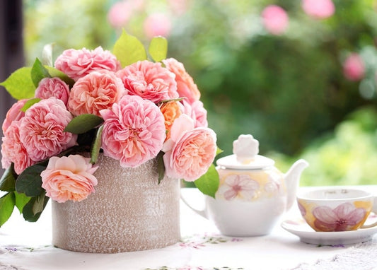 Foto von rosa Gartenrosen im Topf neben einer geblümten Teekanne und Tasse