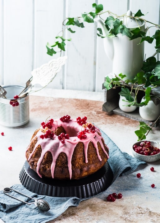 Pink-glazed bundt cake with red currants, ivy, and a linen napkin on a rustic table
