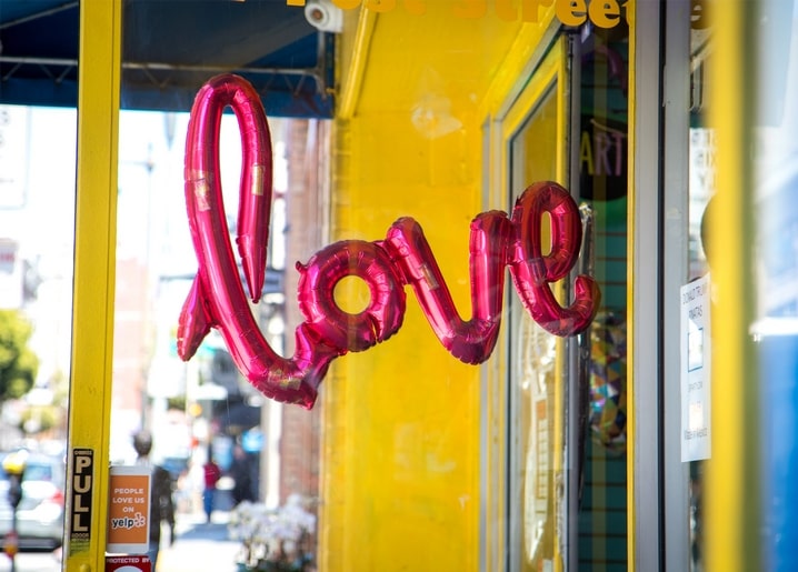 Rosa Folienballon-Buchstaben im Schaufenster eines gelben Ladens