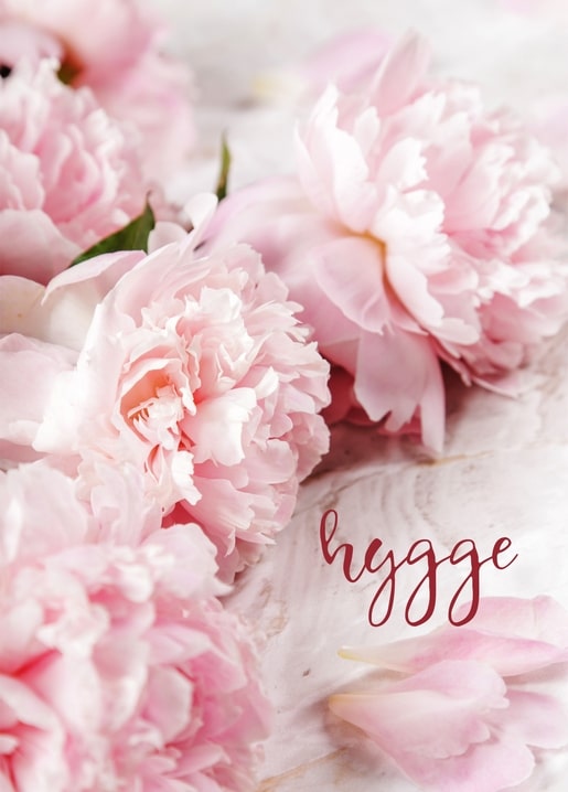 Pale pink peonies with a hand-lettered ‘hygge’ script on a white surface