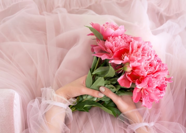 Pink peonies bouquet held in hands wrapped in blush tulle