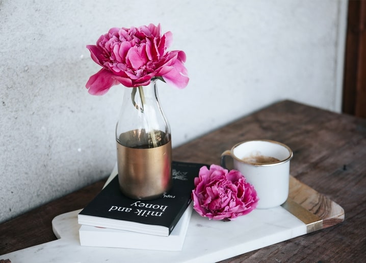 Rosa Pfingstrose in goldbemalter Vase auf Bücherstapel neben einem Milchkaffee