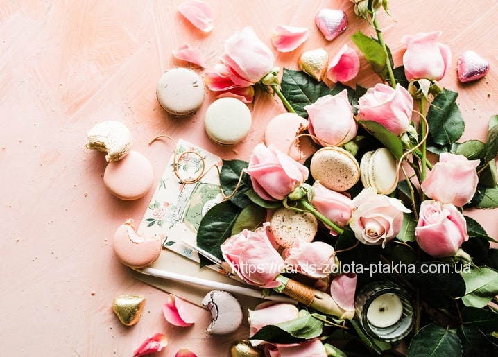 Flat lay of pink roses, pastel macarons, chocolate hearts, and a lit candle