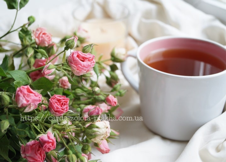 Rosa Strauchrosen neben einer Tasse Tee auf weißem Leinen