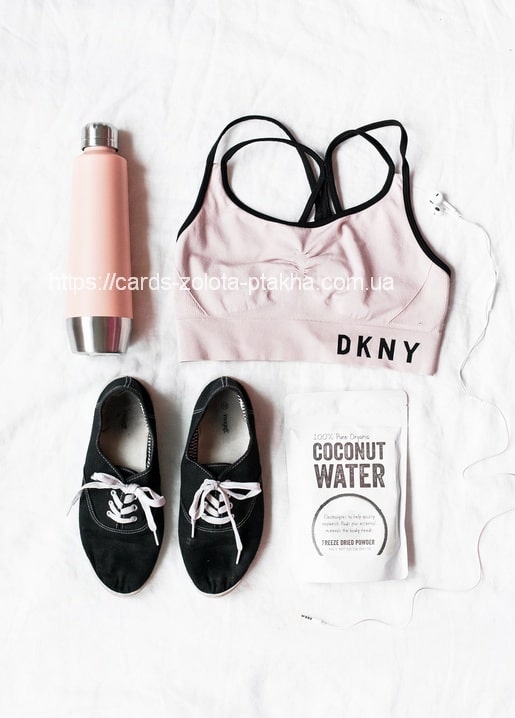 Rosa DKNY-Sport-BH, Wasserflasche, schwarze Sneaker und Kokoswasserpulver als Flatlay.