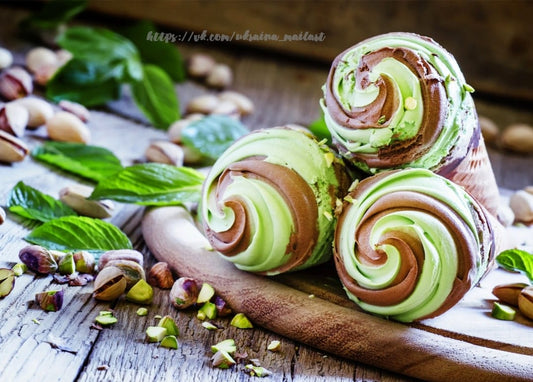 Drei Waffeltüten mit Pistazien-Schoko-Eis, Pistazien und Minze auf einem Holzbrett