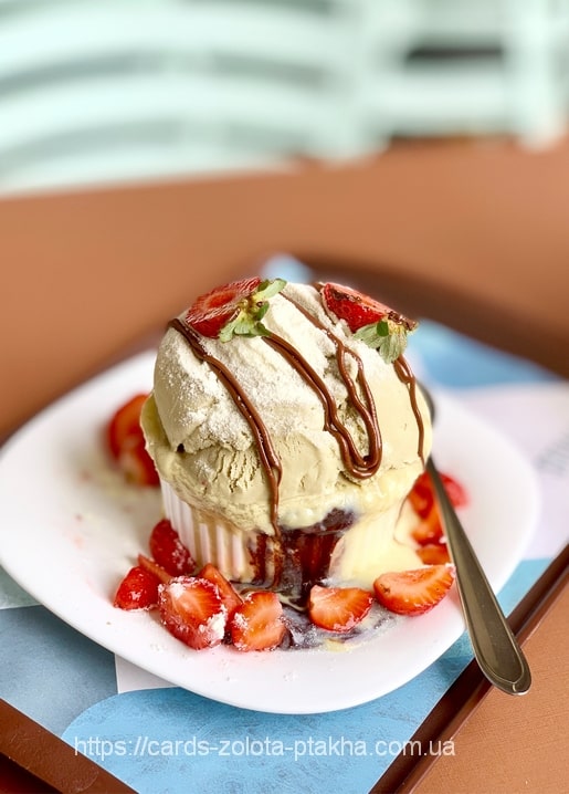 Kugel Pistazieneis mit Erdbeeren und Schokoladensauce auf einem weißen Teller
