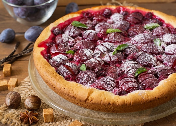Pflaumenkuchen mit Puderzucker, Minze und Pflaumen auf Holztisch